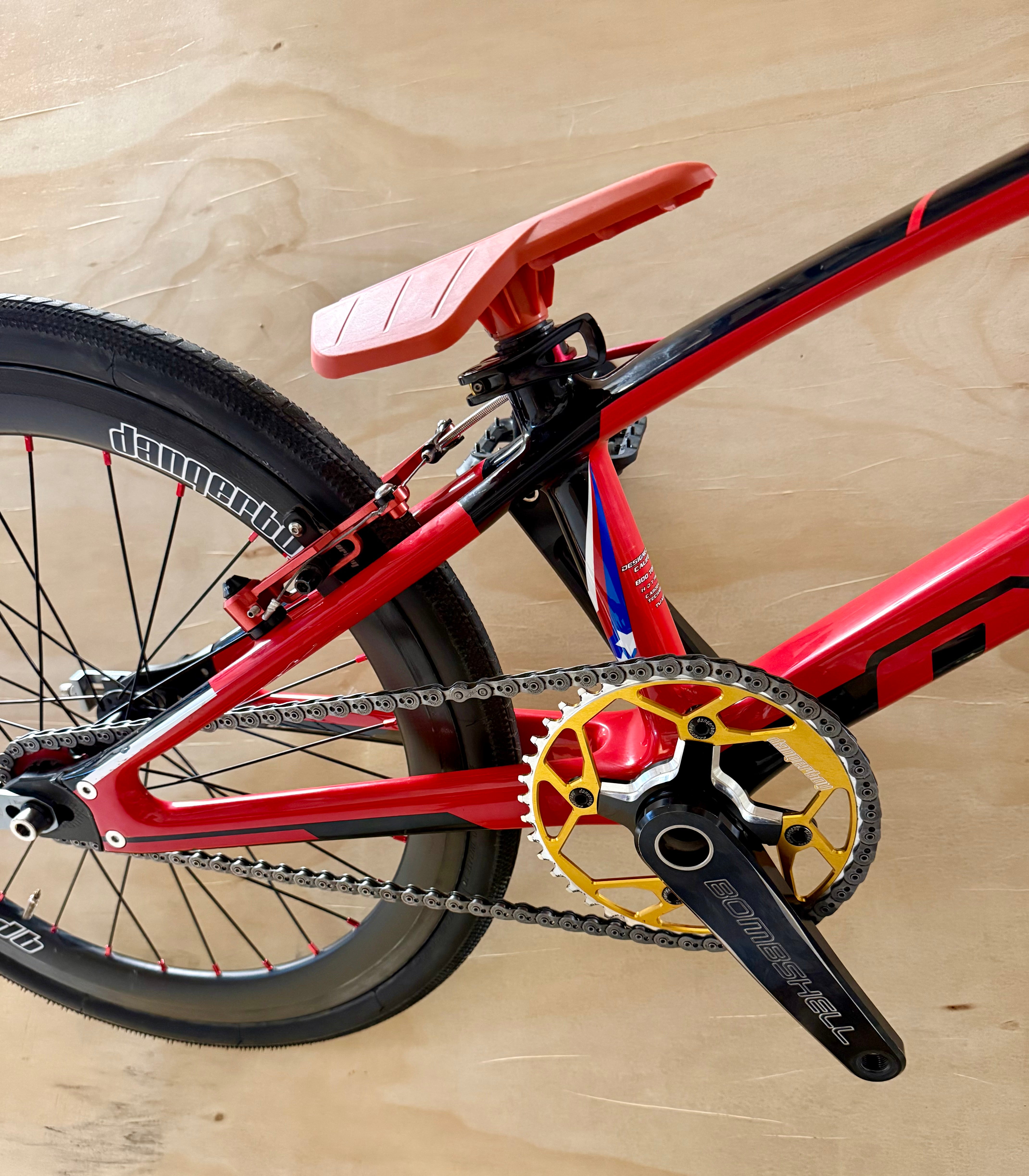 Close-up of a red bicycle with a gold chainring on a wooden surface