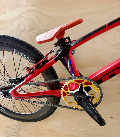 Close-up of a red bicycle with a gold chainring on a wooden surface