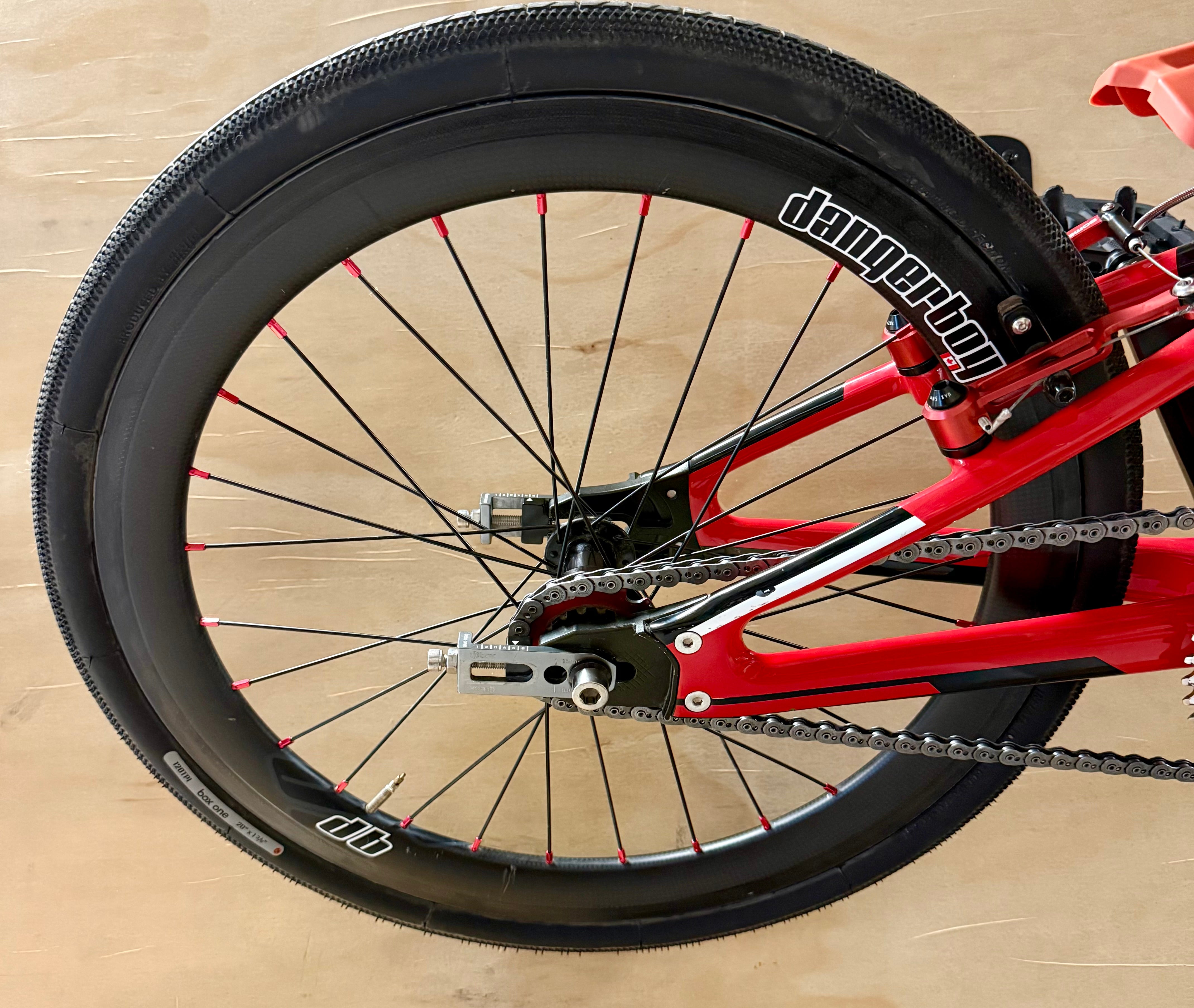 Close-up of a bicycle wheel with red frame and black tire on a wooden floor.