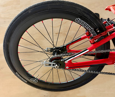 Close-up of a bicycle wheel with red frame and black tire on a wooden floor.